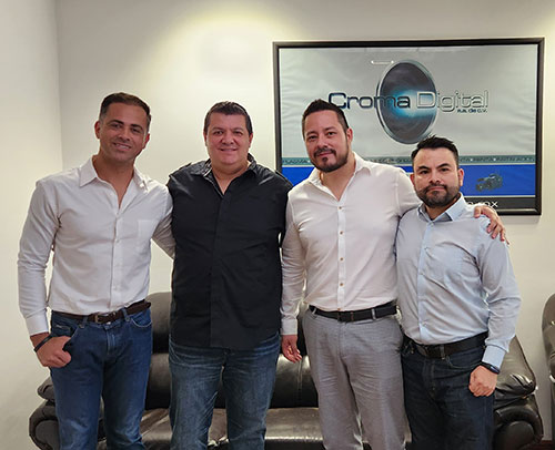 Four men stand together in a small room in fron of a Croma Digital sign.