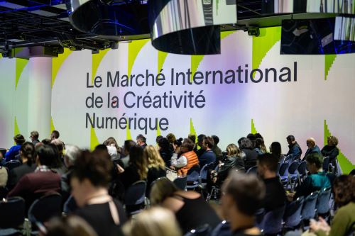 Group of people seated in rows with a floor-to-ceiling sign that reads 'Le March&eacute; International de la Cr&eacute;ativit&eacute; Num&eacute;rique' beside them