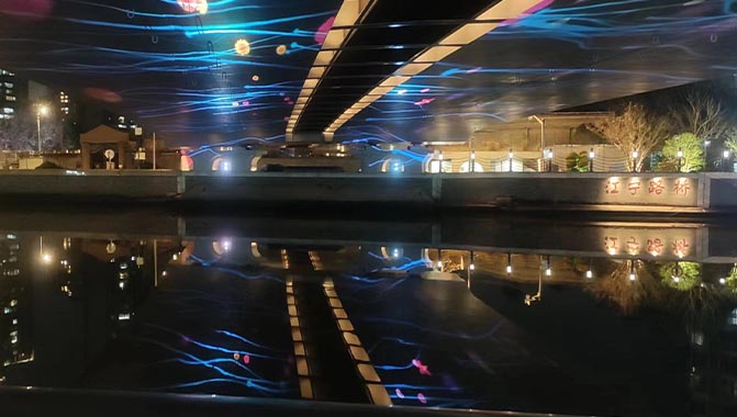 The Illuminated Jiangning Road bridge over Suzhou Creek with lights reflecting on water.