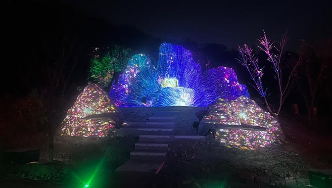 Large rock formations illuminated by colorful projections at night, creating a striking visual contrast against the dark sky.