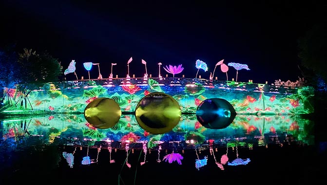 A vibrant stone bridge illuminated with colorful images of flowers, showcasing a lively scene against the night sky.