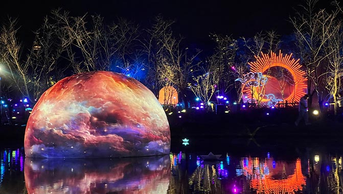 A large sphere on a lake illuminated by projected contents, showcasing an eye-catching and colorful imagery.