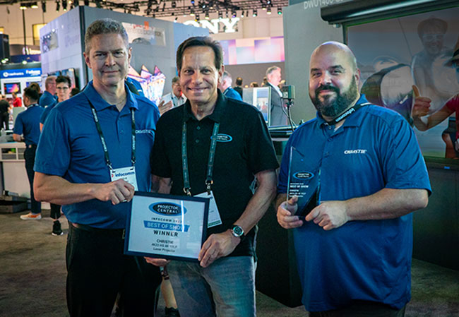     Three men stand side-by-side, with the man in the middle holding an award plaque.