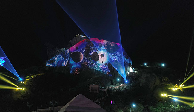 Image planets and meteors projected onto a rocky hill at night.