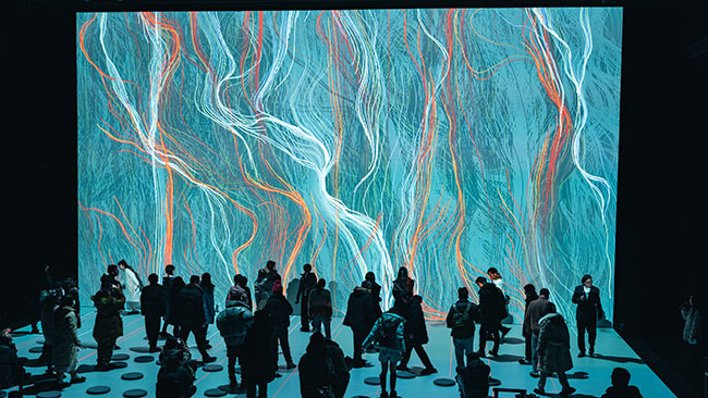 A group of people stand in front of a large screen that displays colorful thread-like imagery.