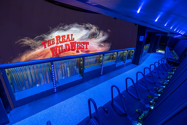 Empty seats in front of a large screen that reads “The real wild west”.