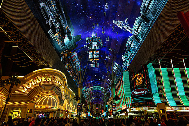 A large LED canopy covers an outdoor shopping and dining area.