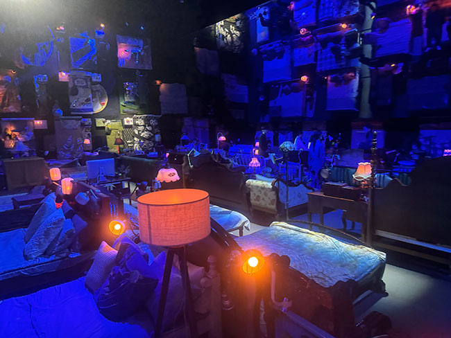 A dimly lit room of beds with side tables and lamps.