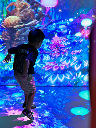 A child explores a room that is projection mapped in vivid colors.