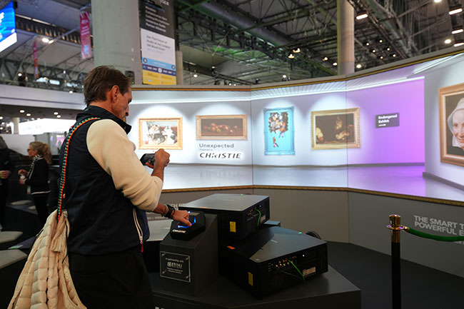 Three projectors light up a three-walled display with an art-gallery-inspired image.