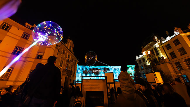 People watch a projection mapping show on the façade of a building.