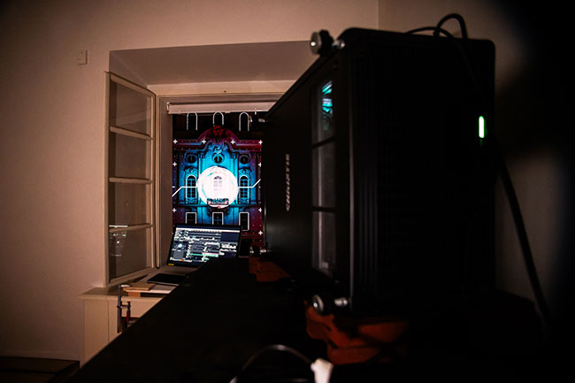 View of a Christie projector illuminating a building through an open window. 