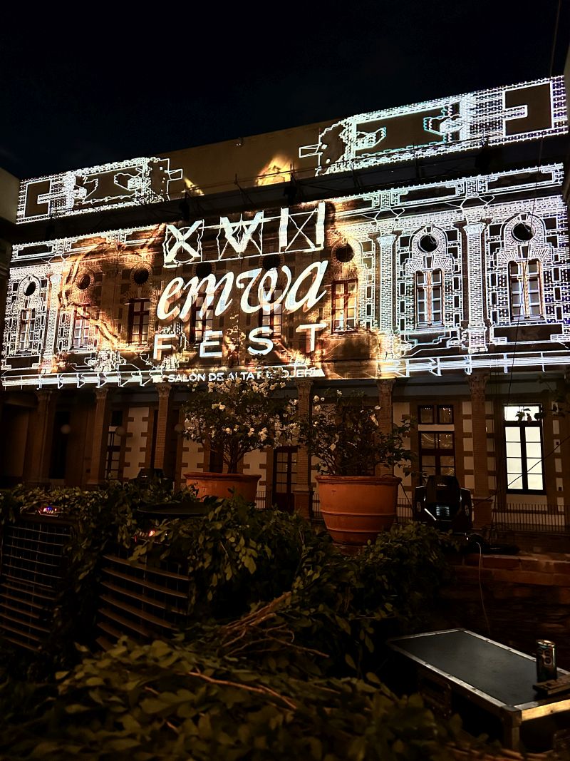 An elaborate indoor façade is surrounded by plants and projection mapped with an intricate black and white design.