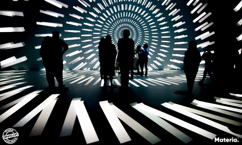 People shown in relief against walls and floor with a black and white projected pattern. 