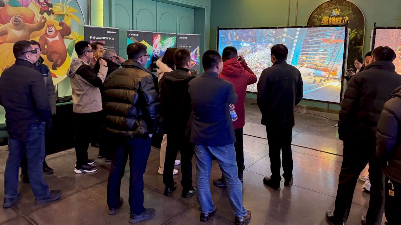 A group of people stand in front of a large screen displaying a vibrant projected image. 