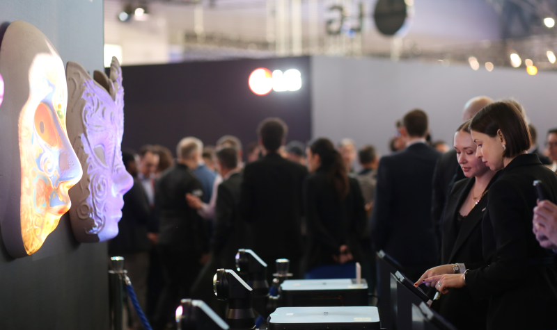 Two women look at a touch panel in front of projection mapped masks.