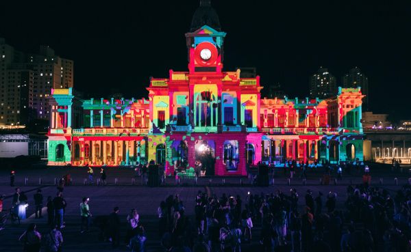 The fa&ccedil;ade of a large building is projection mapped with vibrant colors.
