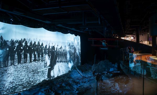 A large indoor screen shows a projected image of soldiers on a battlefield.